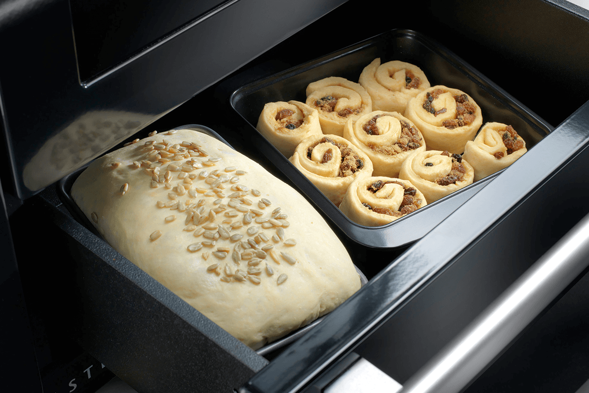 Some bread with seeds on top and some cinnamon scrolls sit in the Falcon cooker proving drawer waiting to be cooked. 