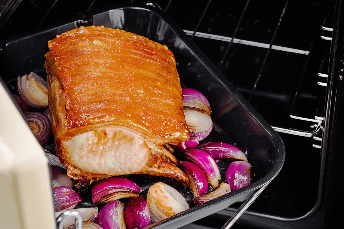 The oven door is open with the Falcon Handyrack detail being shown with a roasting pork on a bed of onions.