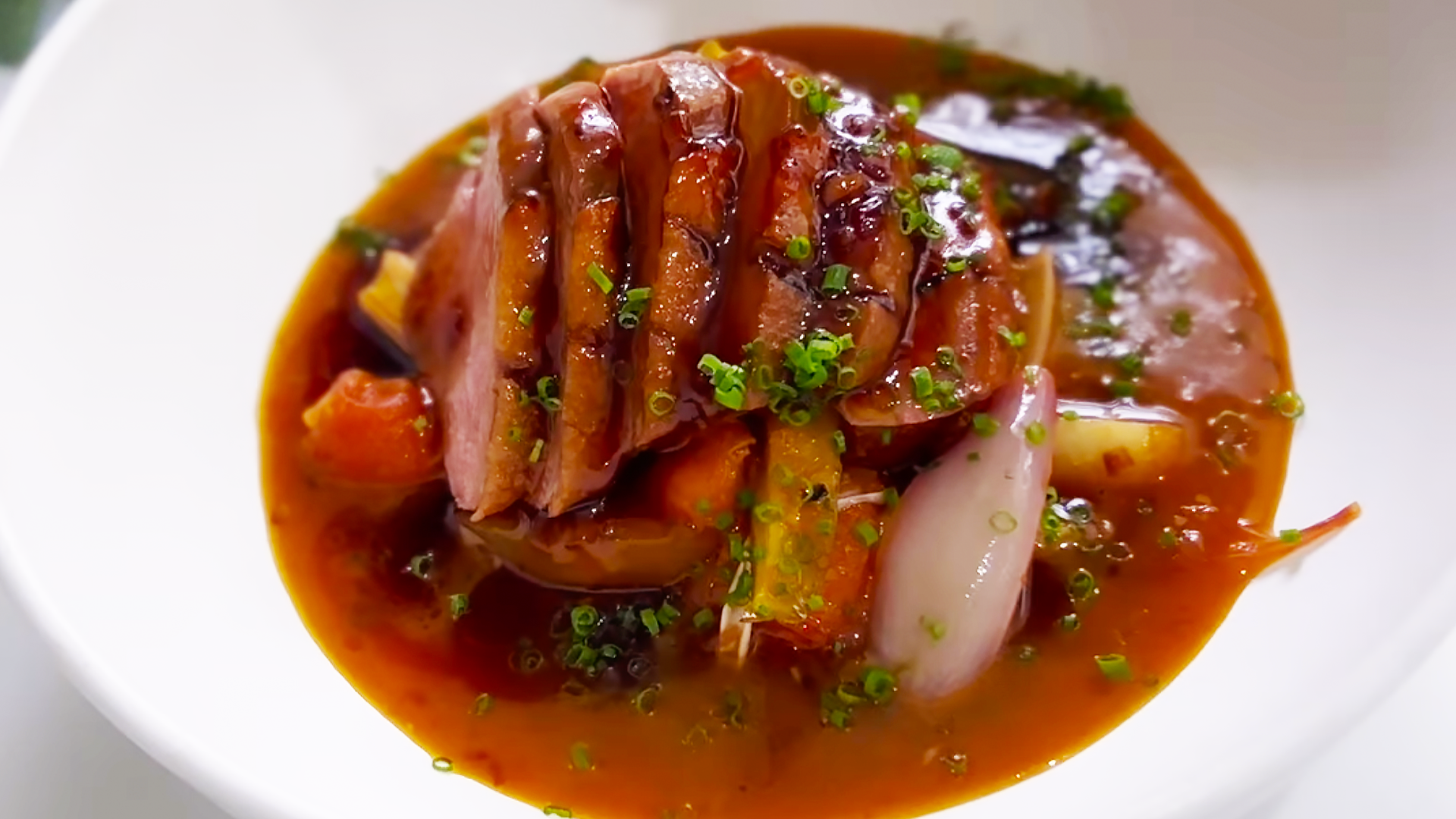 Sliced duck breast in an Asian sauce with vegetables sits on white plate.