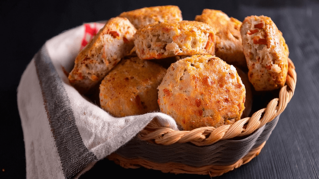 A wicker basket with a teatowel, sits on a benchtop with freshly baked parmesan cheese scones.