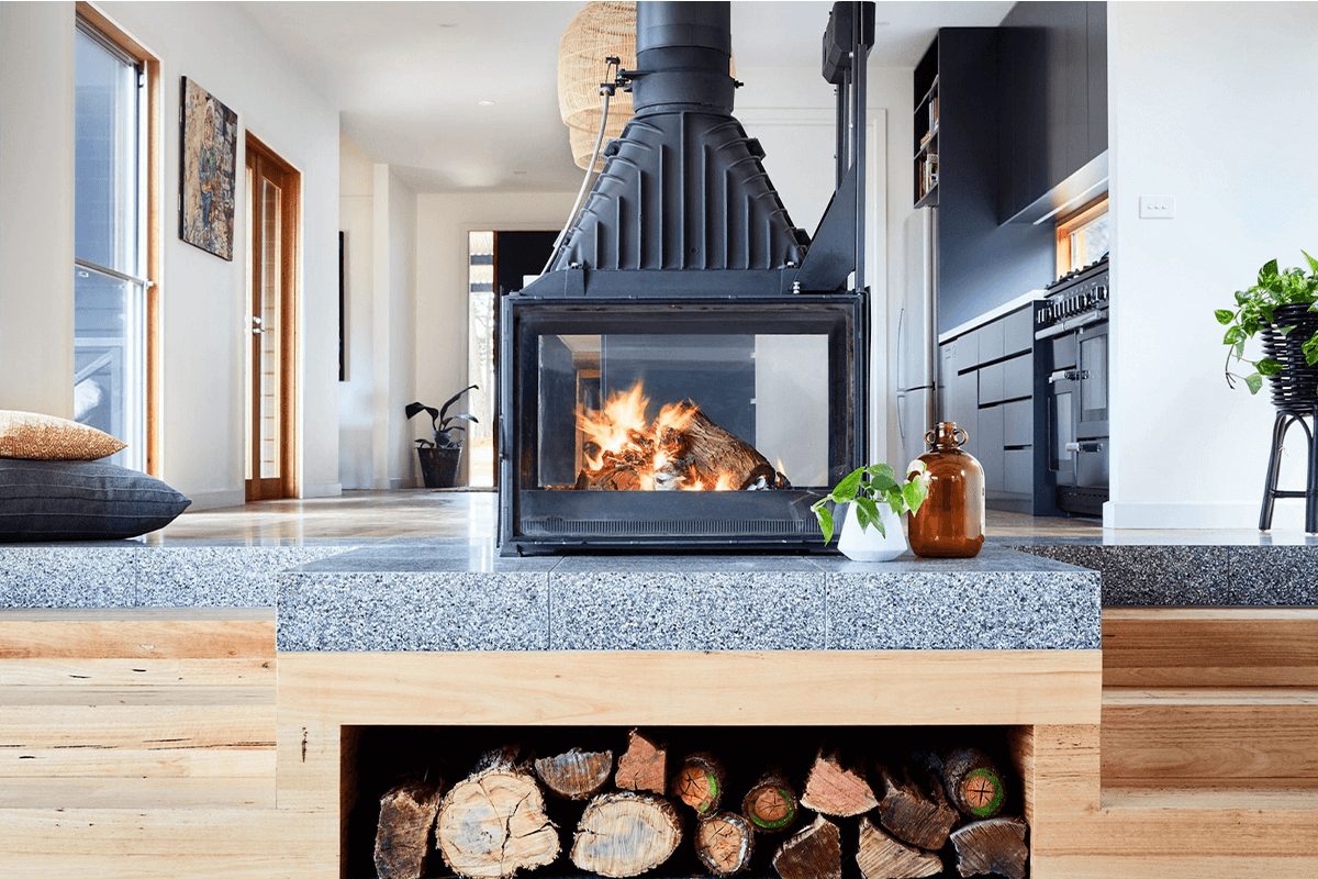 A Cheminées Phillipe fireplace sits in the middle of an open planned modern living space with on stone hearth with stacked wood underneath.