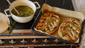 A white pot of pea and mint soup, sits on the top of a Falcon Elise stove top next to a tray of freshly baked fougasse bread, golden brown and coverered in herbs and walnuts.